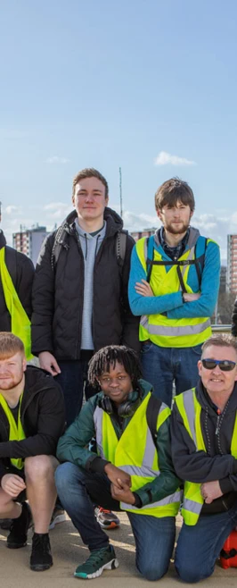 A group of civil engineering students and lecturers posing for a group photo on the Stockingfield Bridge, all wearing high-visibility vests with a cityscape in the background. A group of civil engineering students and lecturers posing for a group photo on the Stockingfield Bridge, all wearing high-visibility vests with a cityscape in the background.